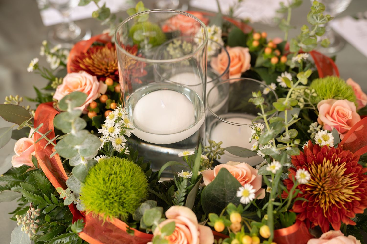 Elegant autumn floral centerpiece with coral dahlias, peach roses, and green chrysanthemums on a rustic table setting.