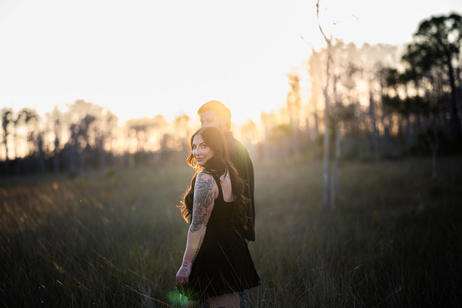 Silhouette of person in dark clothing against warm sunset glow through trees in outdoor setting.