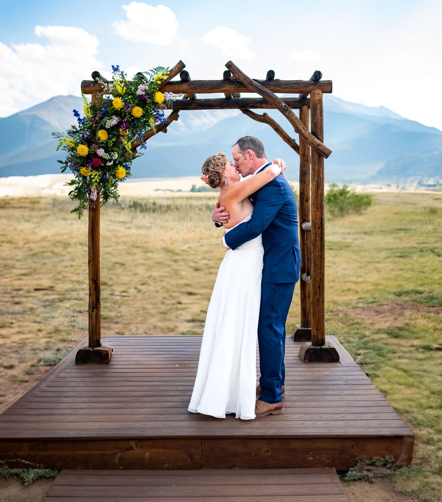 Wedding ceremony under a wooden arch with mountain views and floral decorations.