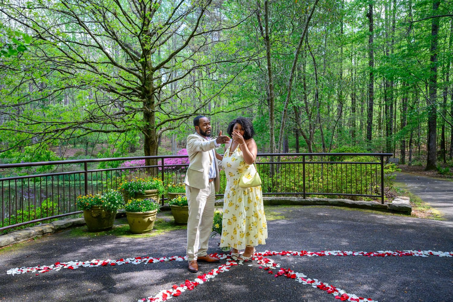 A joyful couple stands together on a petal-decorated patio in a wooded garden, celebrating a romantic proposal moment.
