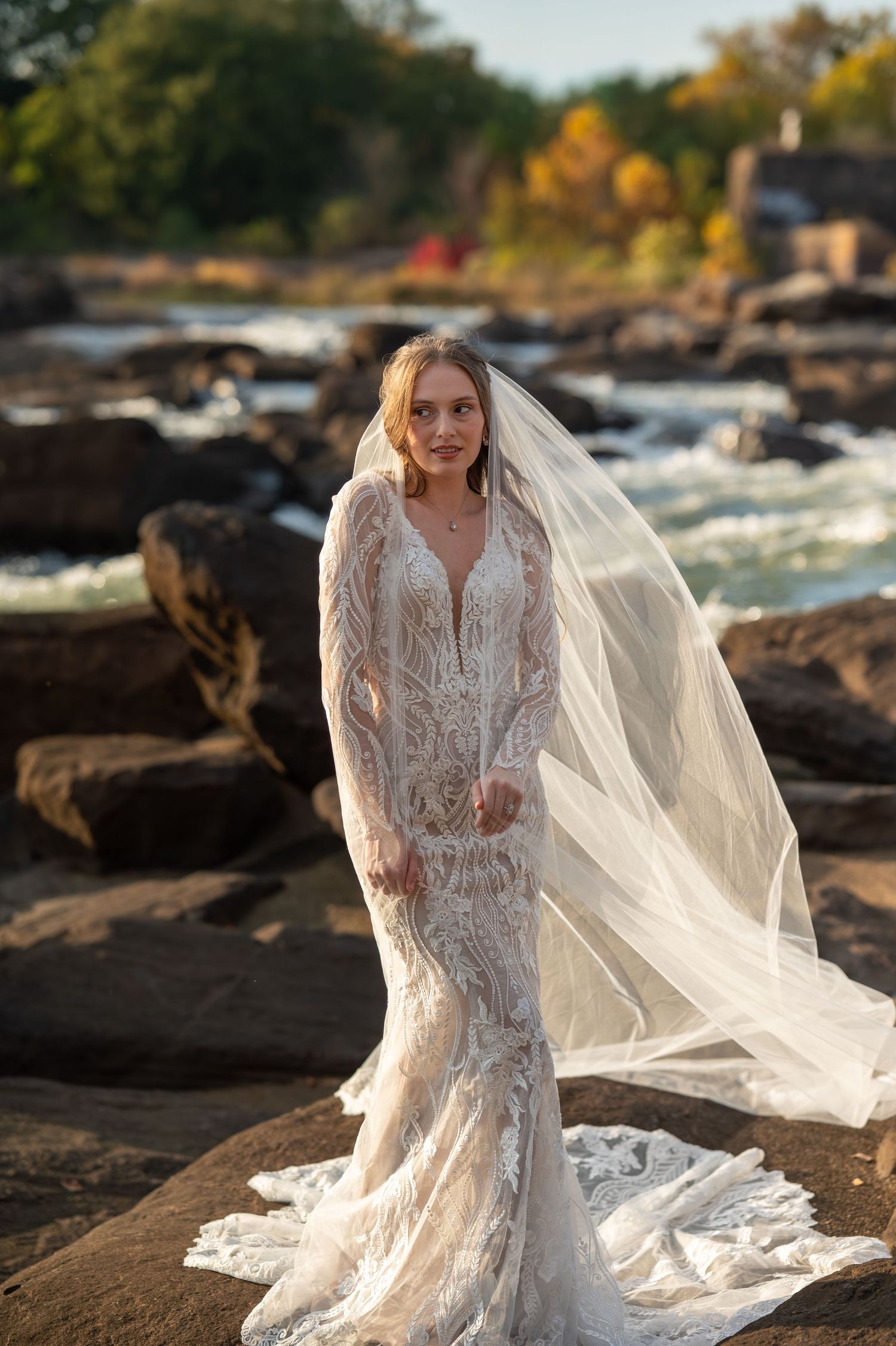 A stunning lace wedding dress with flowing veil captured in a series of sunset photos by a rocky waterfront.