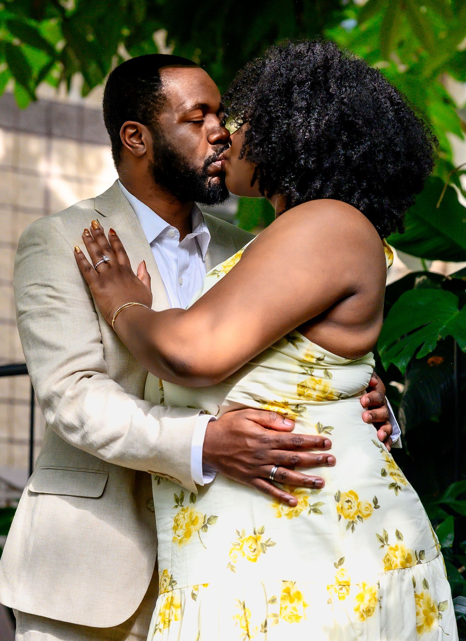A couple sharing an intimate kiss indoors surrounded by lush tropical greenery.