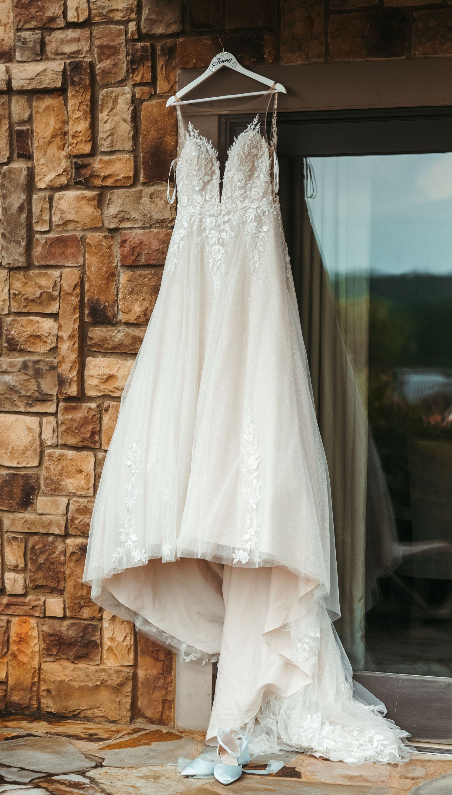 Elegant white lace wedding dress hanging on display against a stone wall.