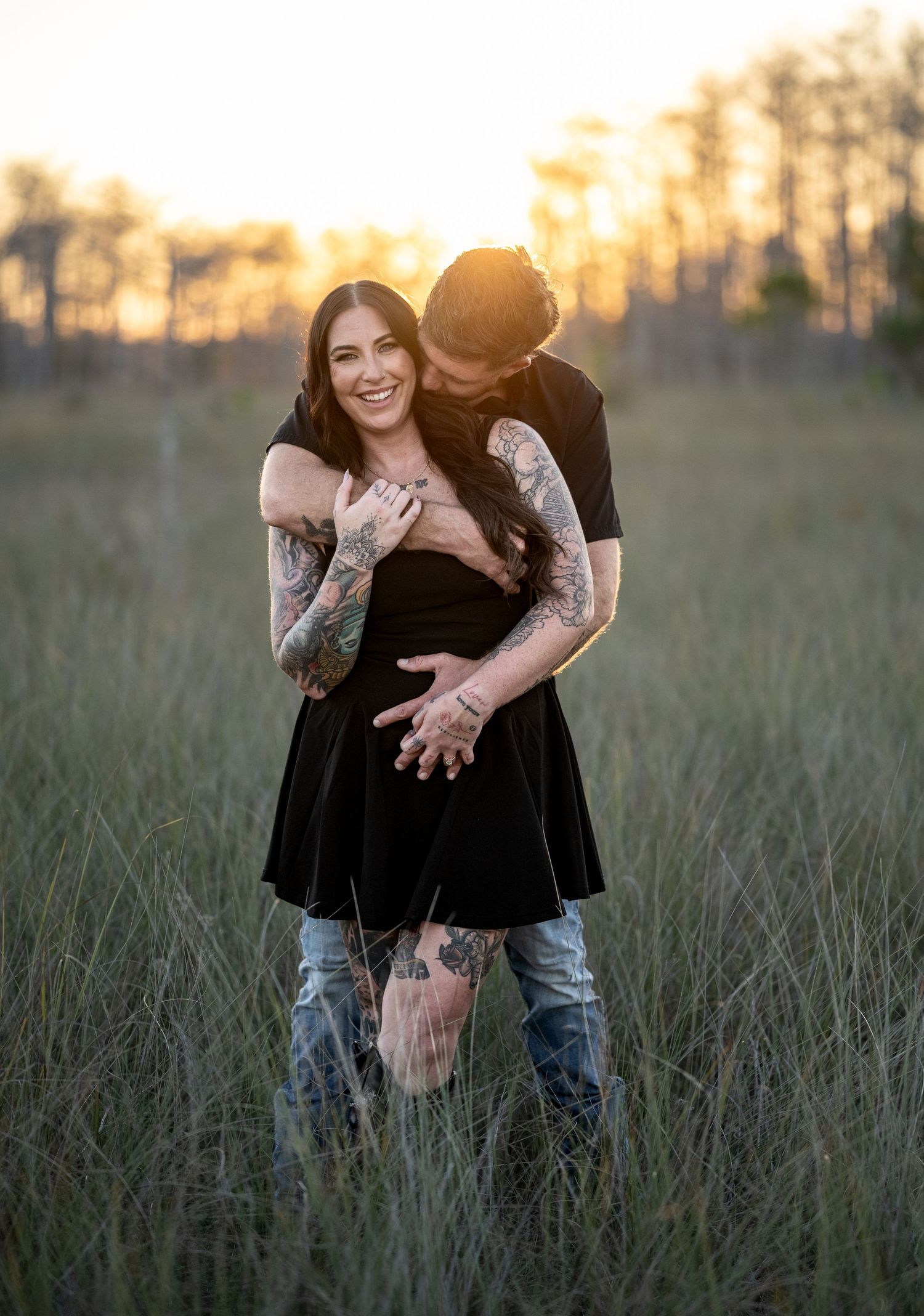 Playful couple shares intimate moments in tall grass at sunset.