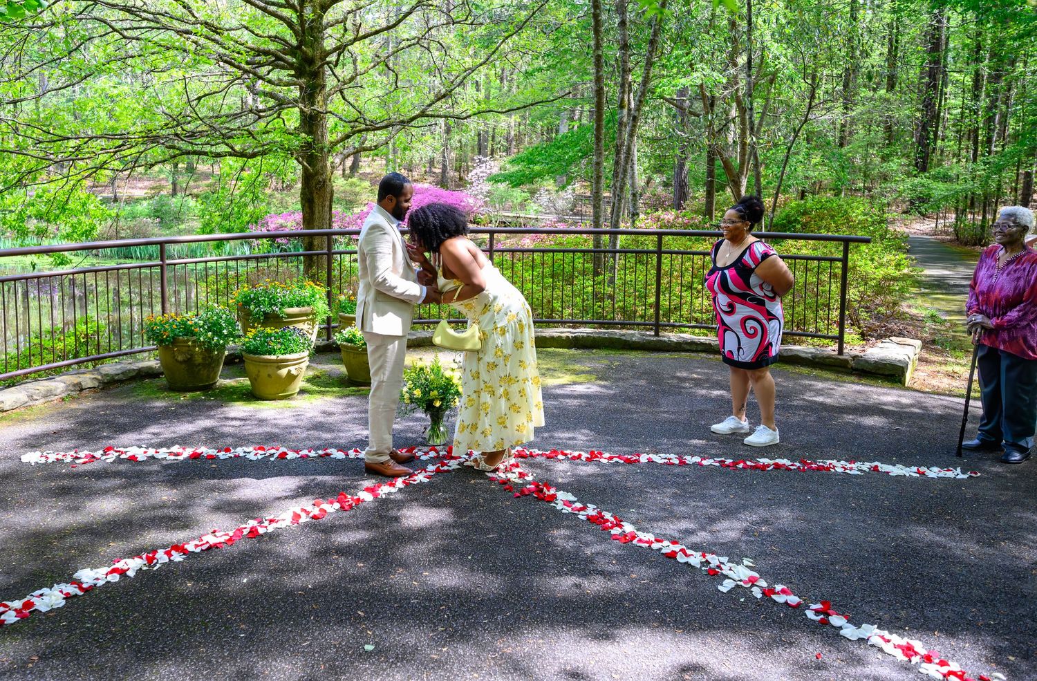 Outdoor wedding ceremony with couple exchanging vows on a petal-decorated path surrounded by lush green trees.