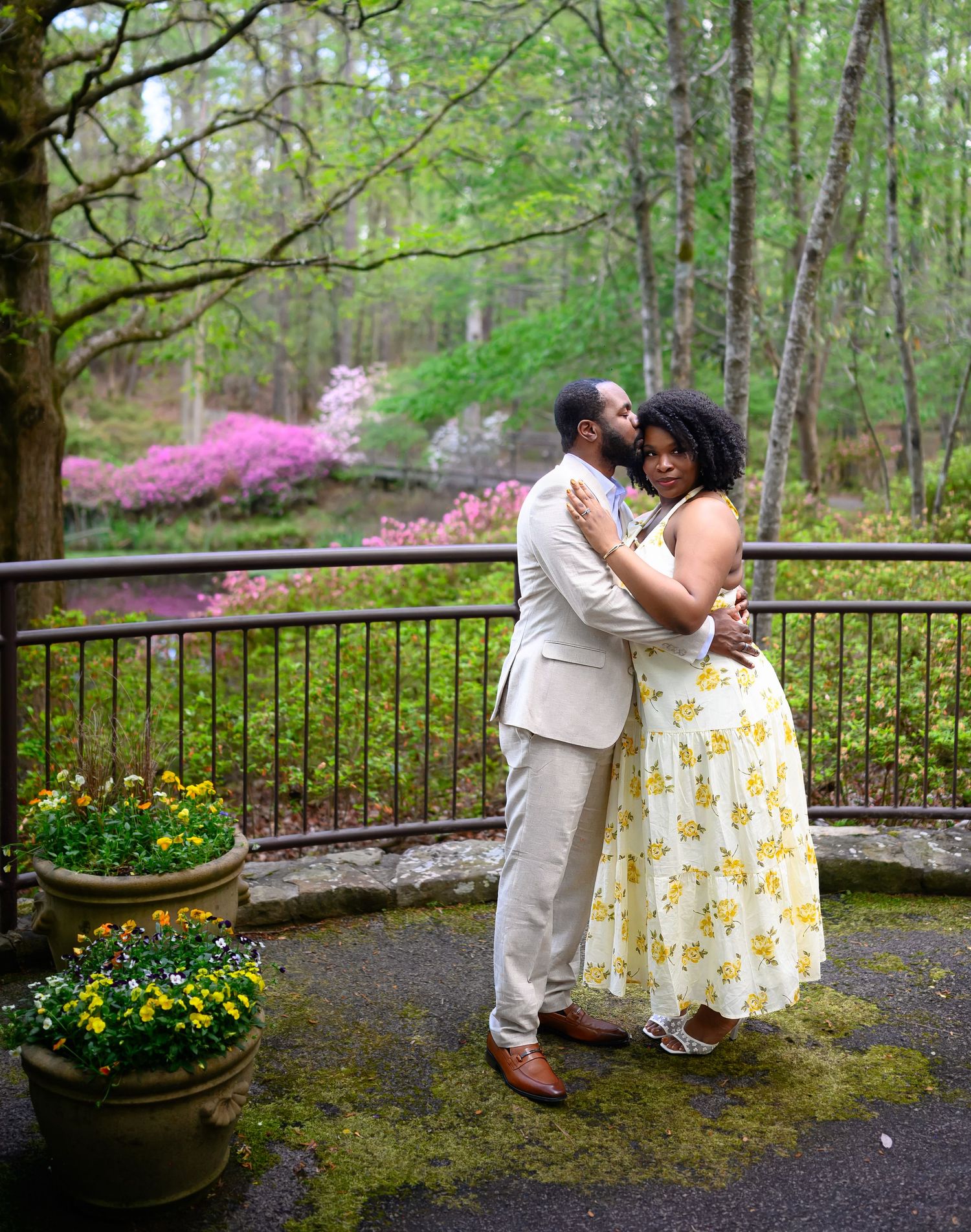 Romantic couple embracing on a mossy terrace surrounded by blooming azaleas and lush green forest backdrop.