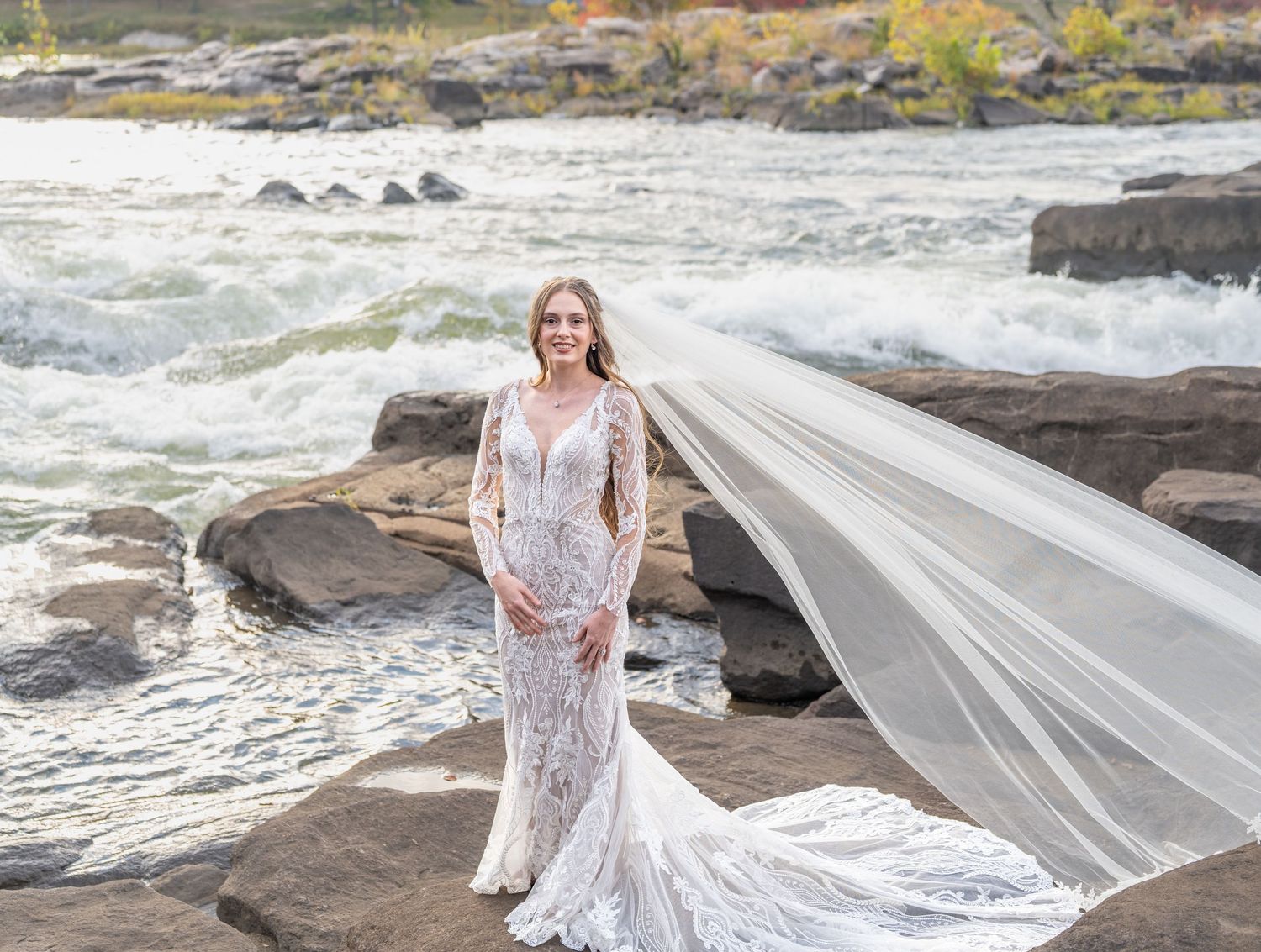 A flowing white wedding dress billows in the wind against dramatic coastal rocks and crashing ocean waves.