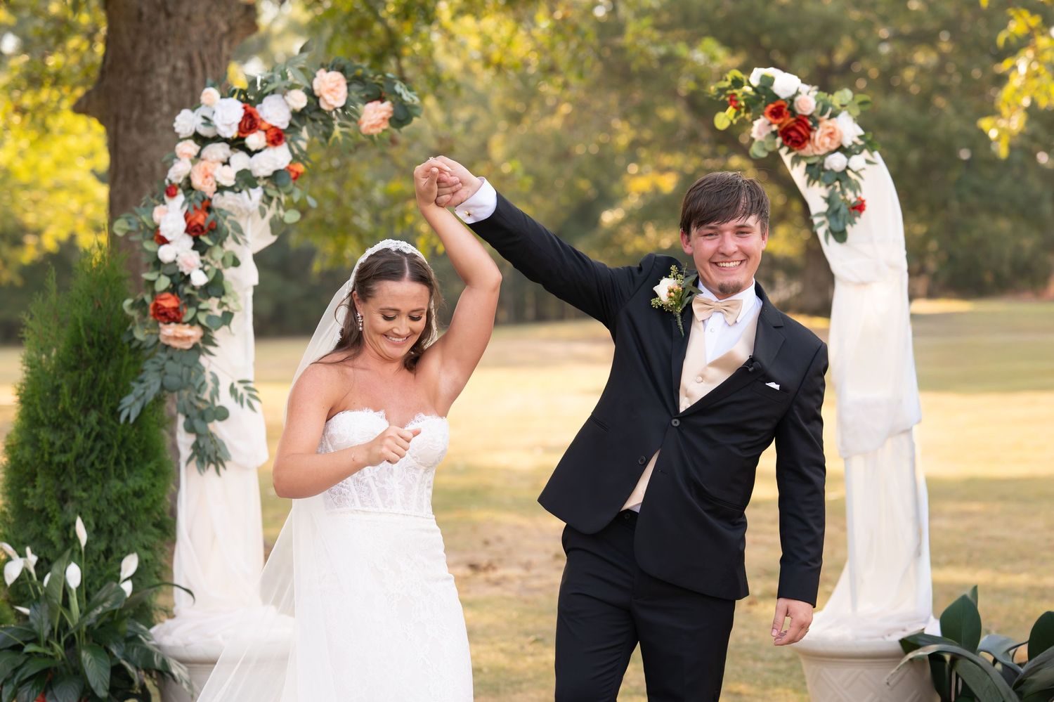 Wedding ceremony setup with floral arrangements and white decor in a natural outdoor garden setting.