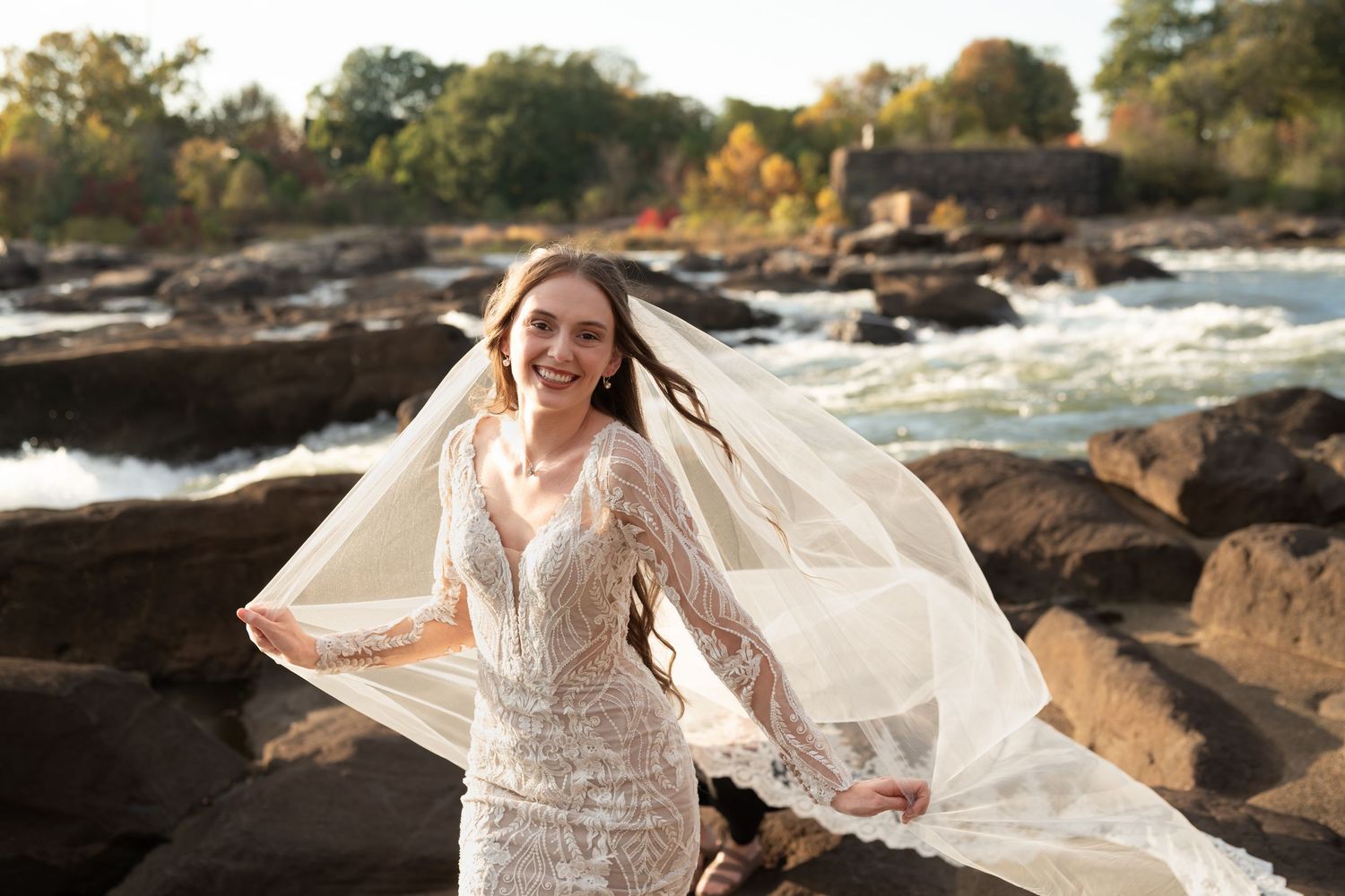 Ethereal bridal portrait with flowing veil against scenic autumn landscape and rushing water.