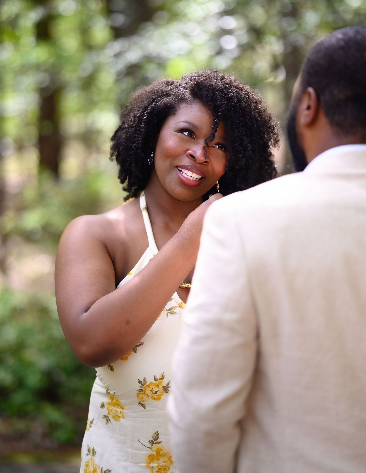 Smiling Black woman in a yellow floral dress gazes lovingly at her partner during a garden proposal.