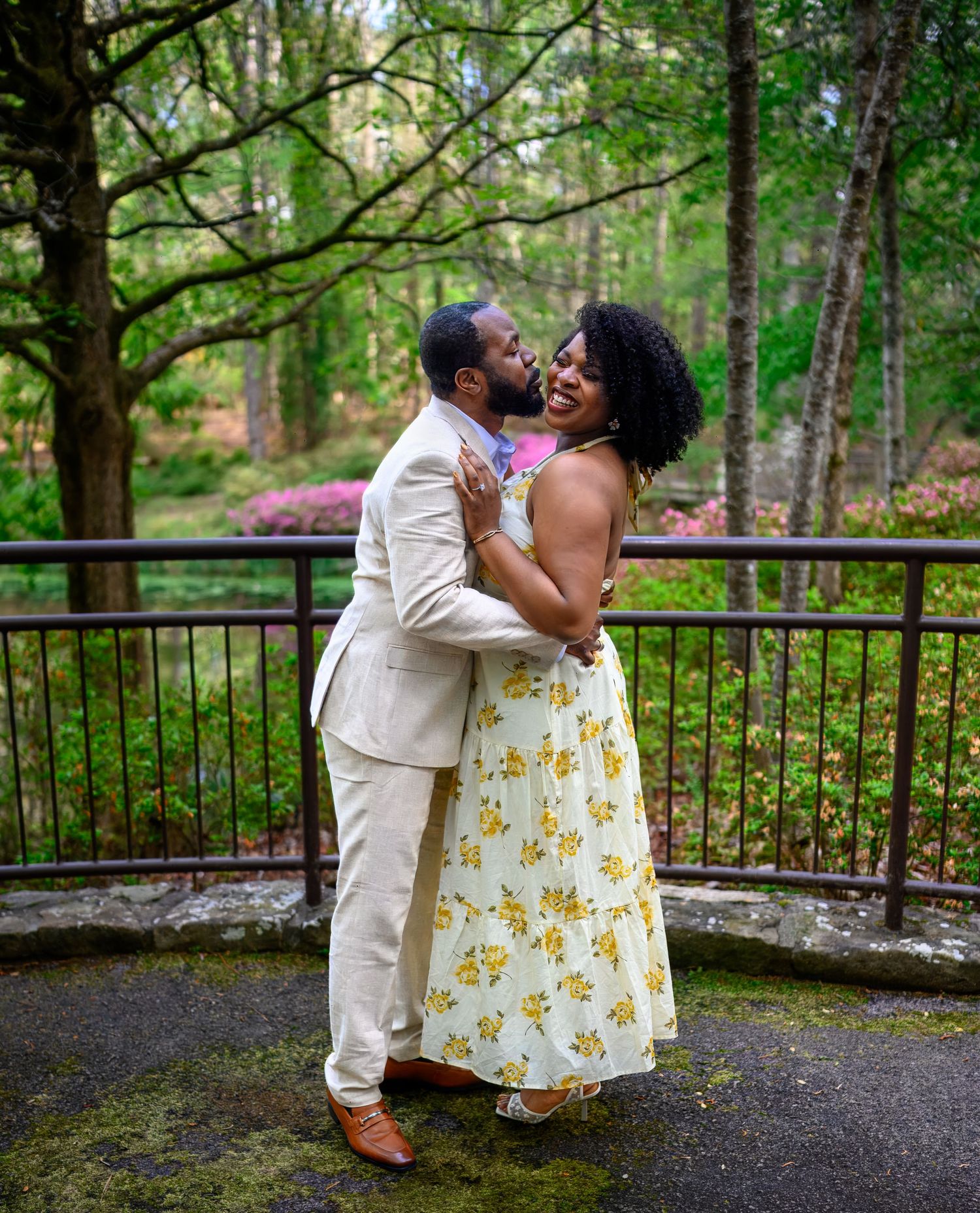 A couple shares a romantic embrace on a stone terrace surrounded by colorful spring foliage.