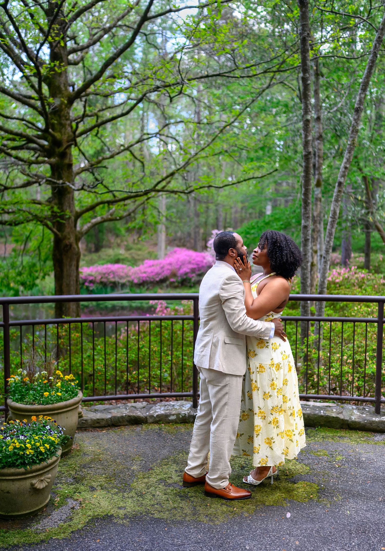 Couple sharing a romantic moment on a garden terrace with colorful azaleas and lush greenery in the background.