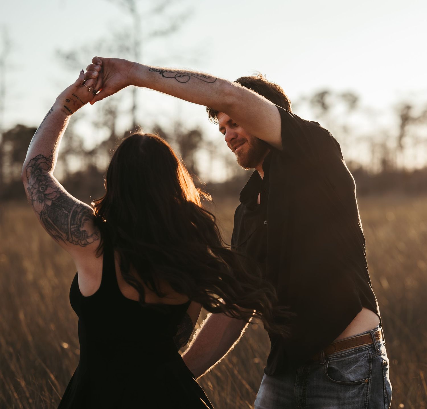 Couple sharing an intimate moment in a golden field at sunset with dramatic lighting.