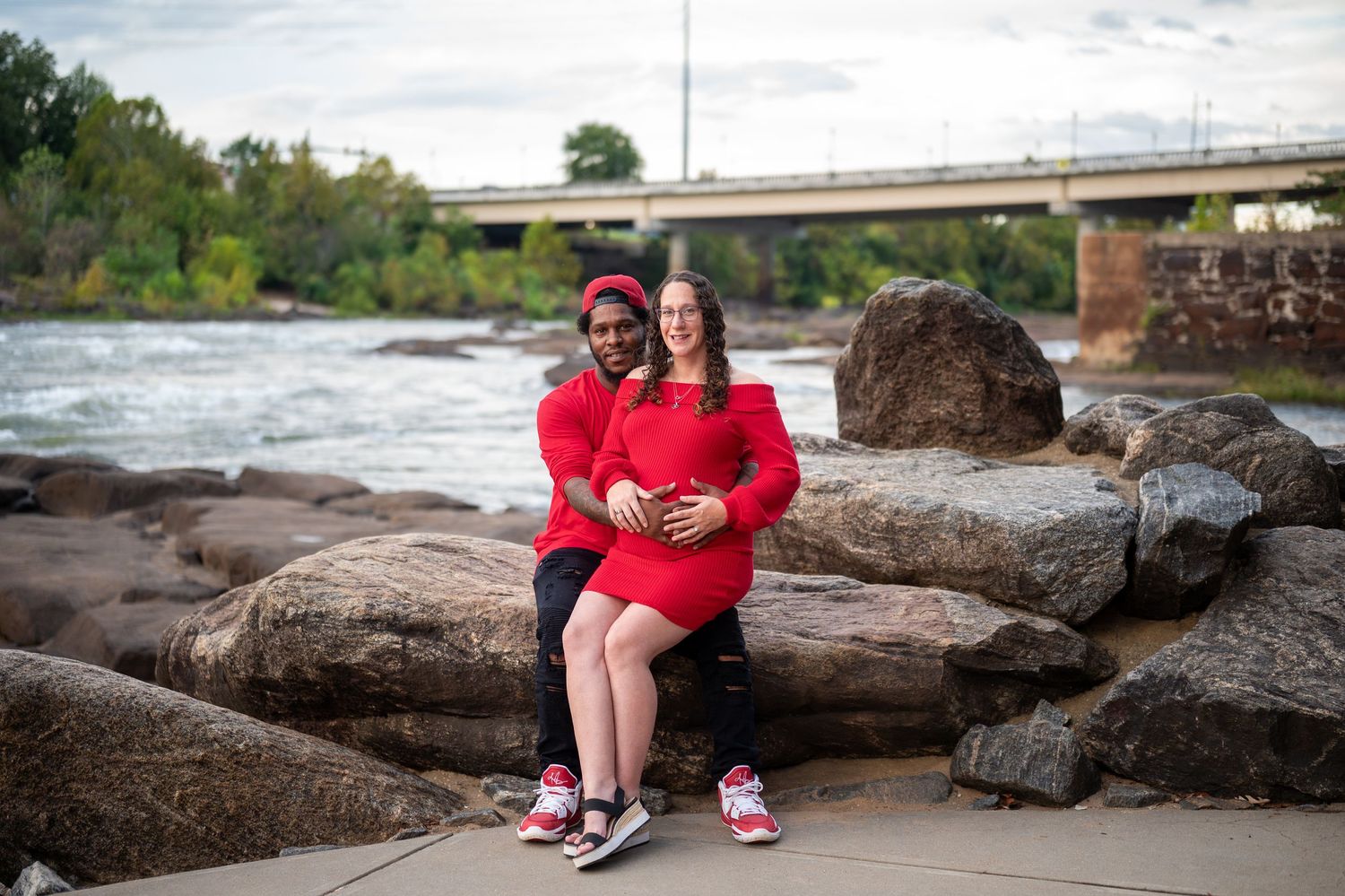 Family members in bright red clothing pose together on large rocks by the water's edge.