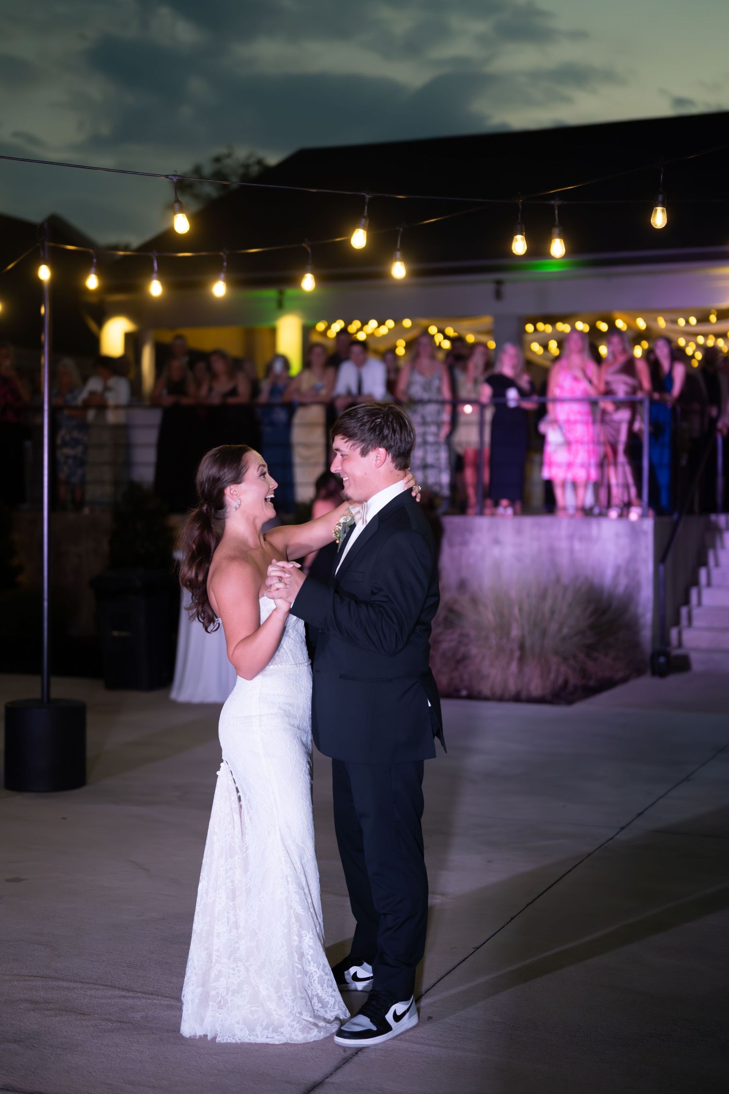 A couple shares their first dance at an evening wedding reception under glowing string lights.