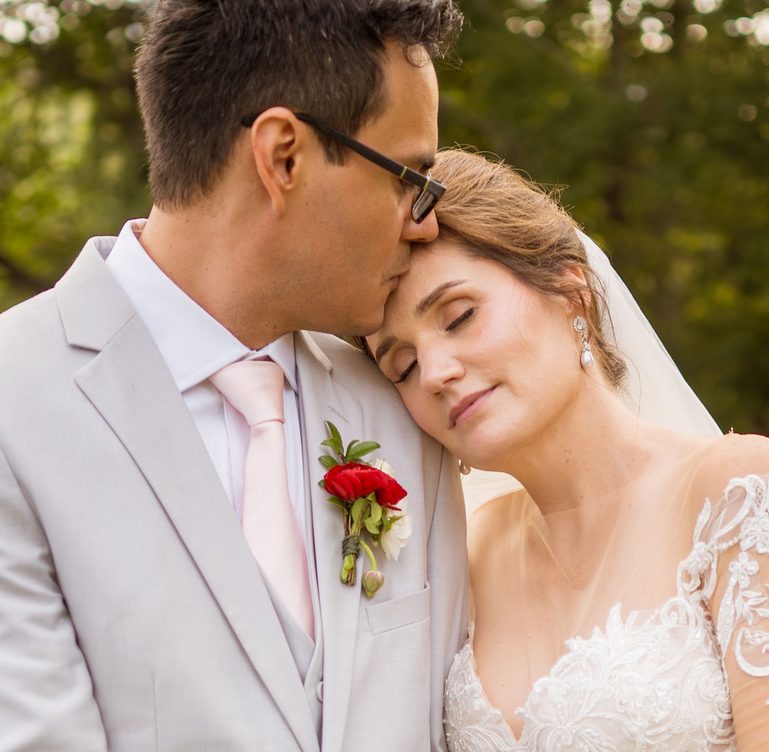 Intimate romantic close-up portrait of newlyweds in a garden setting, with the groom in a gray suit and pink tie.