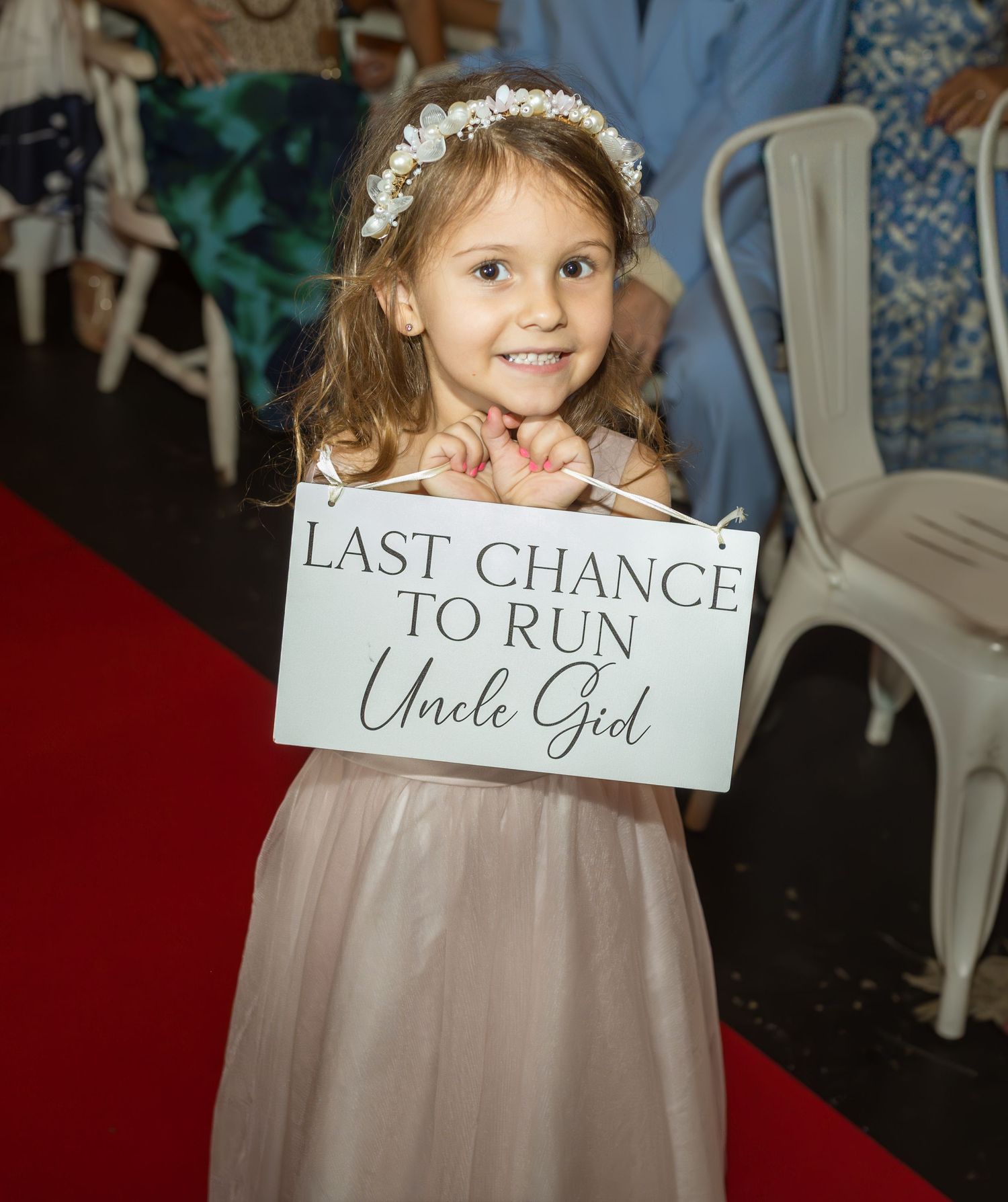 A young flower girl in a pink dress holds decorative wedding signs.