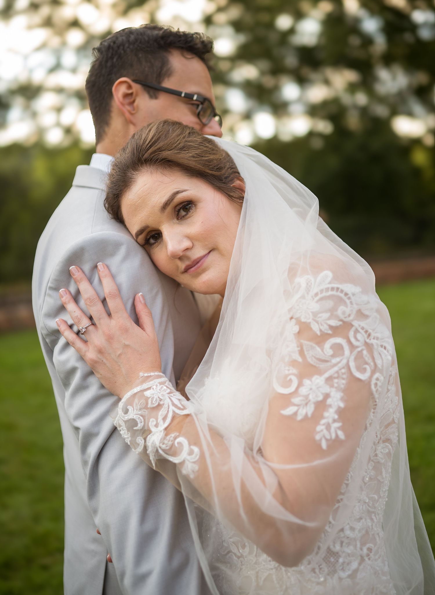 Wedding couple embracing outdoors showing intricate lace veil details.
