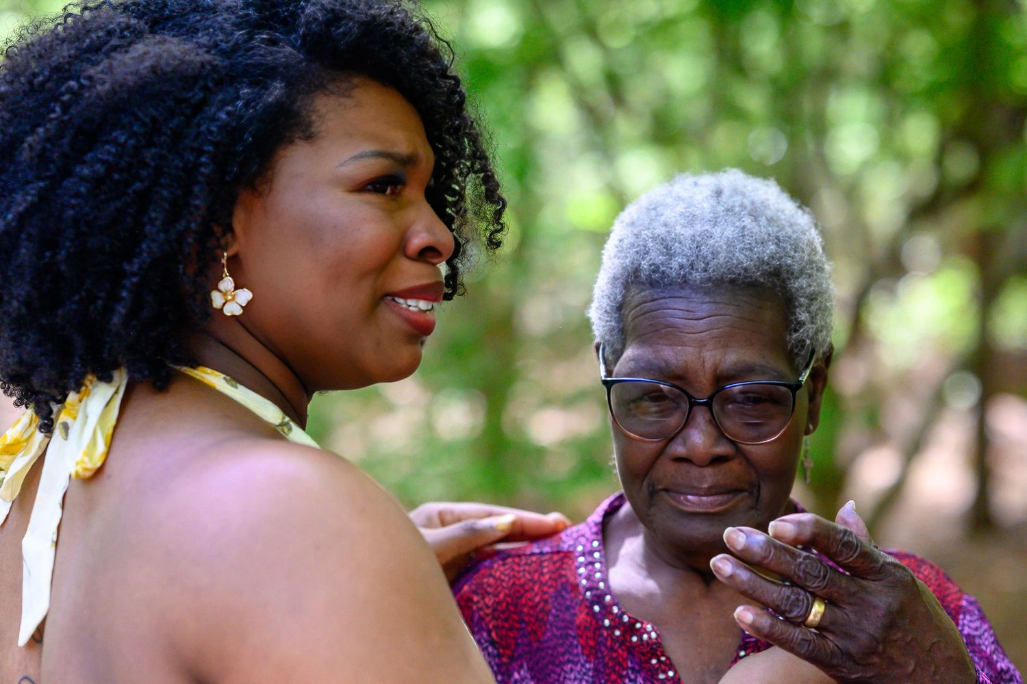 Young woman comforting elderly woman at outdoor wedding celebration.