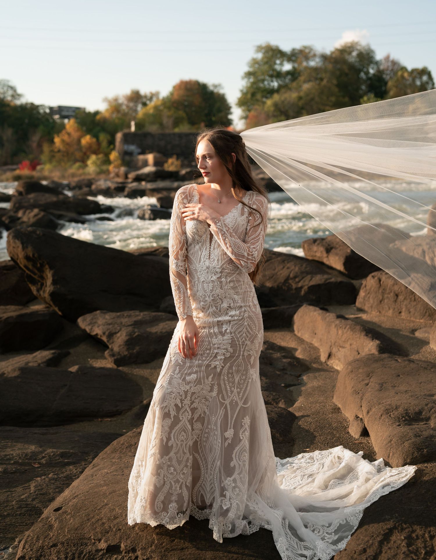 Dramatic bridal portraits on rocky terrain with a detailed lace gown and cathedral veil catching sunlight.