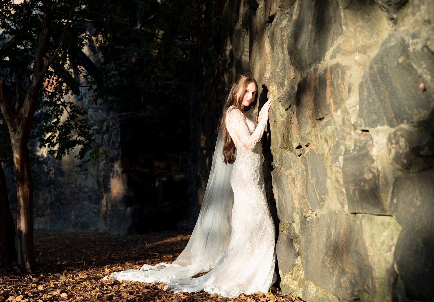 Dramatic bridal photos against stone walls showcasing an elegant lace wedding dress with cathedral veil.