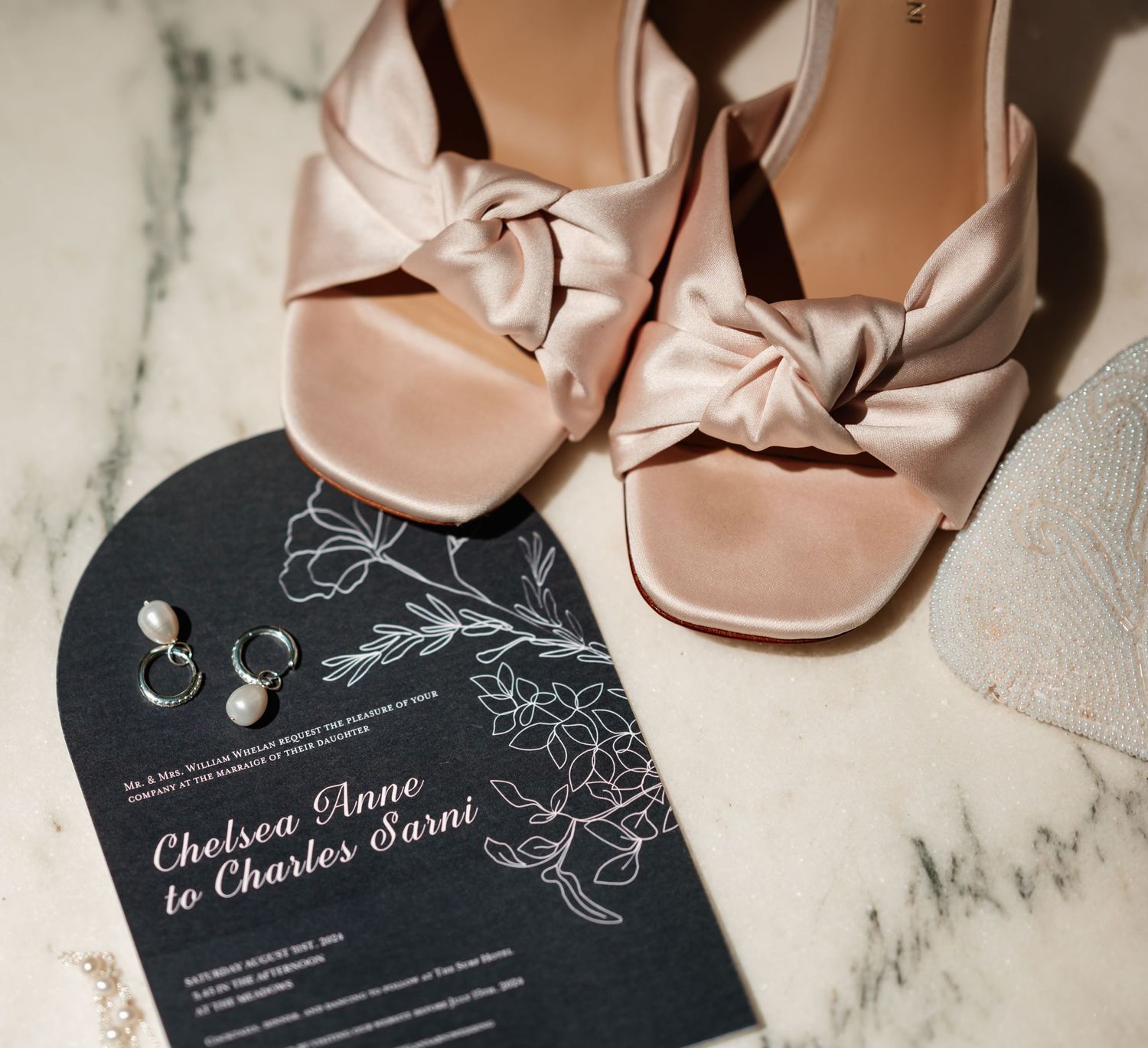 Blush pink wedding shoes with elegant black and white invitation suite on marble surface.