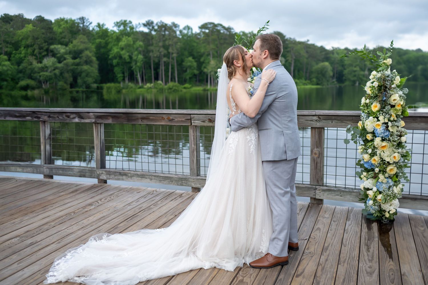 Wedding party poses on a wooden deck overlooking a scenic waterfront.