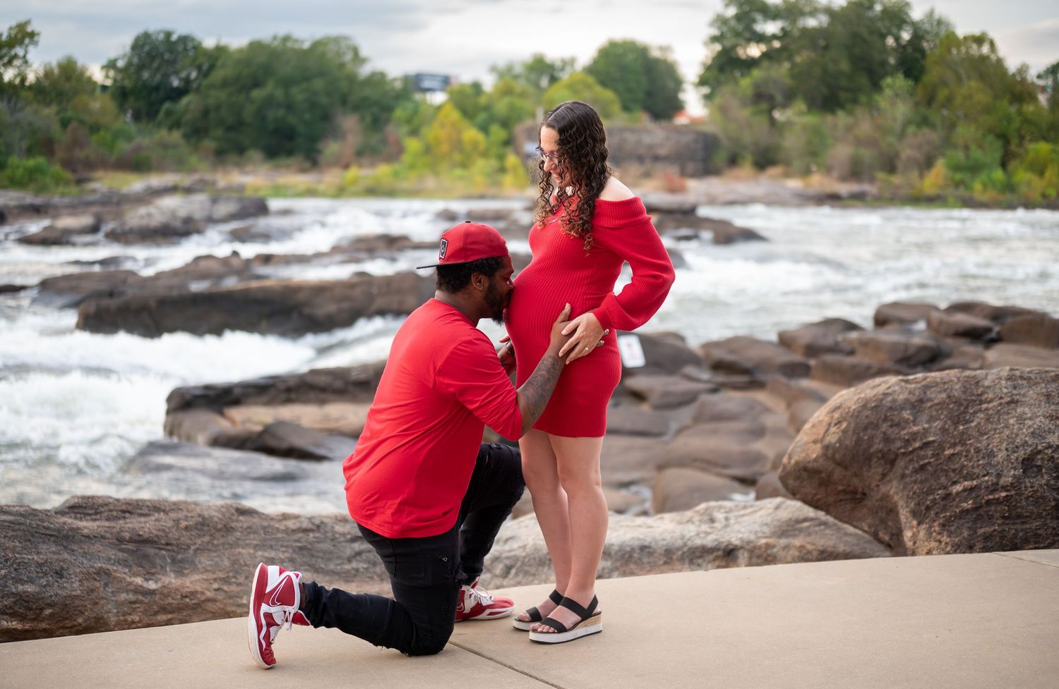 Scenic engagement photos taken on rocky shoreline with couple in coordinated red outfits against natural backdrop.