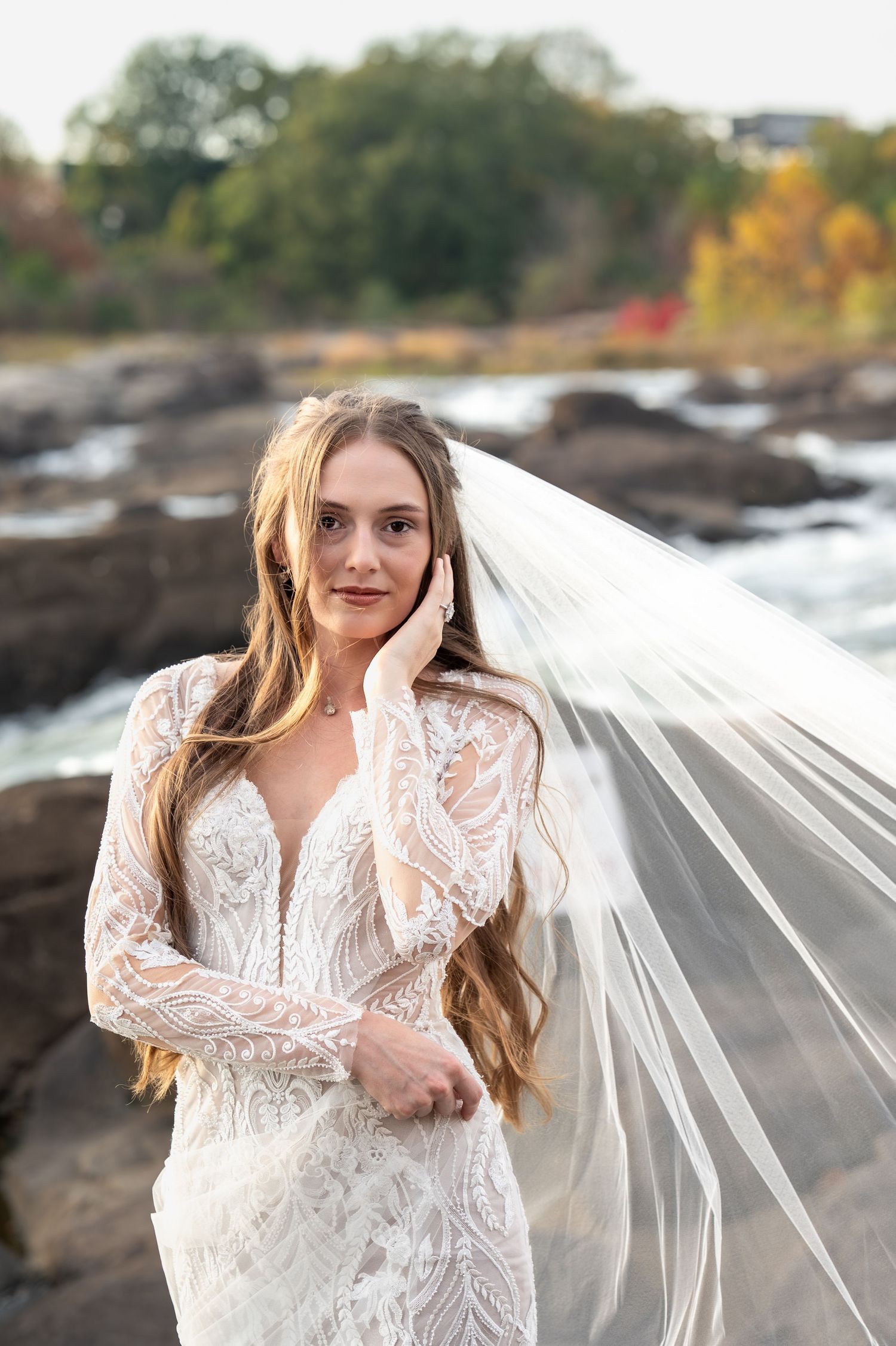 A flowing white lace wedding dress photographed against rocky coastal scenery at sunset.