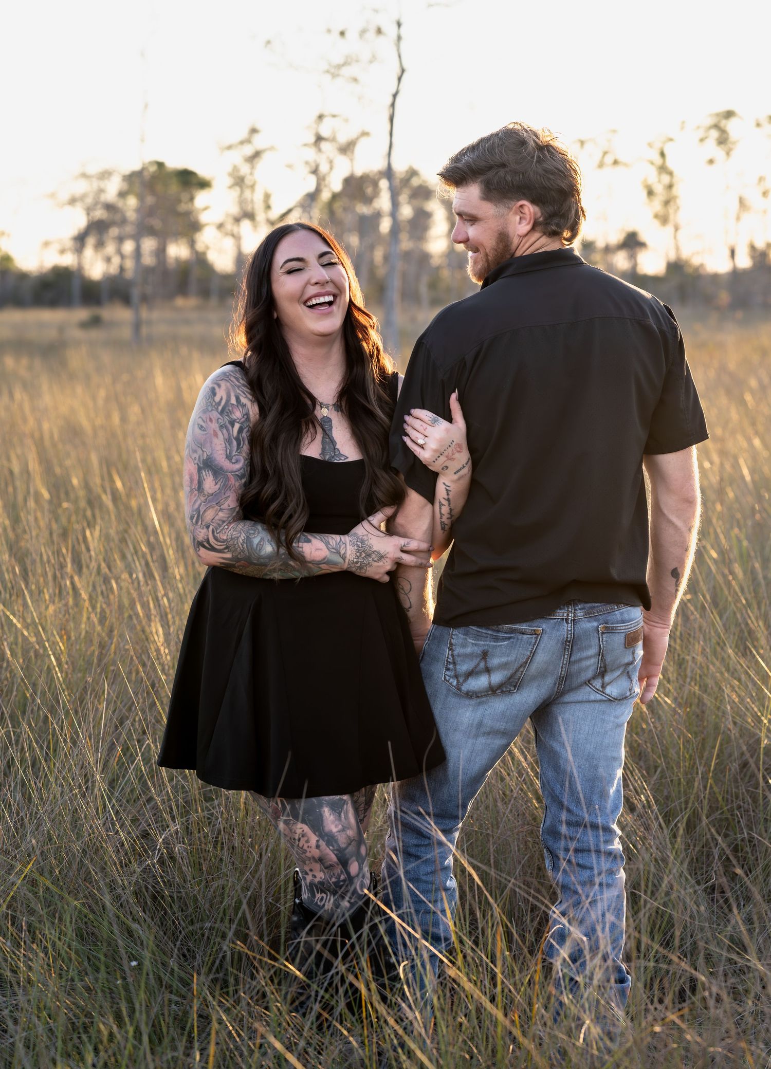 Romantic couple laughing together in a golden sunlit field of tall grass.