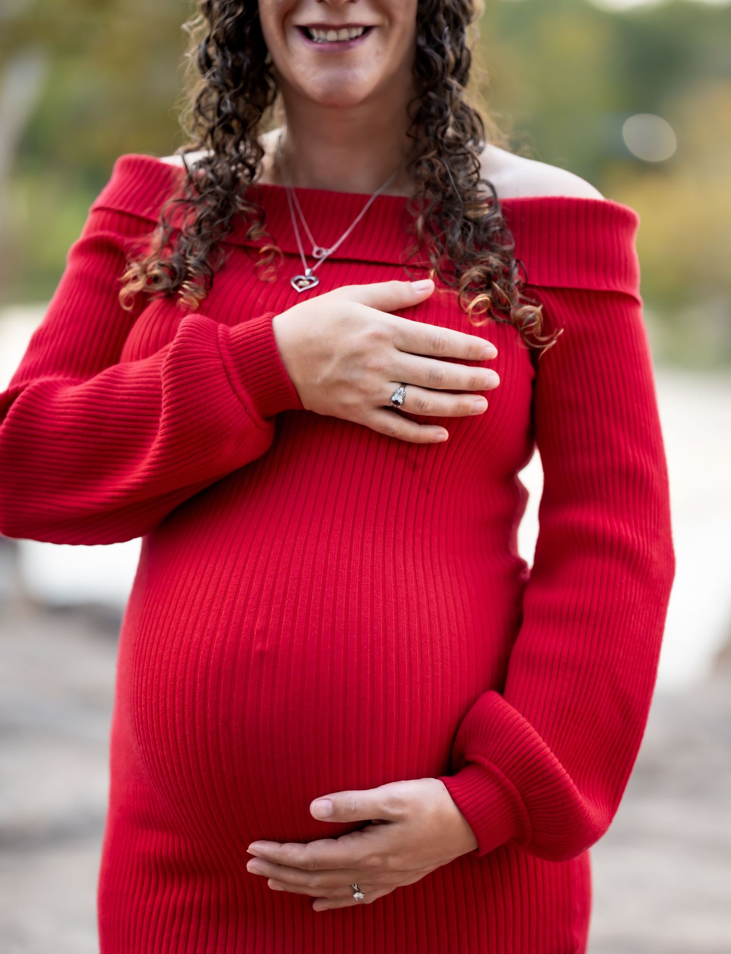 Close-up of pregnant belly in fitted red sweater dress with hands gently cradling the bump.