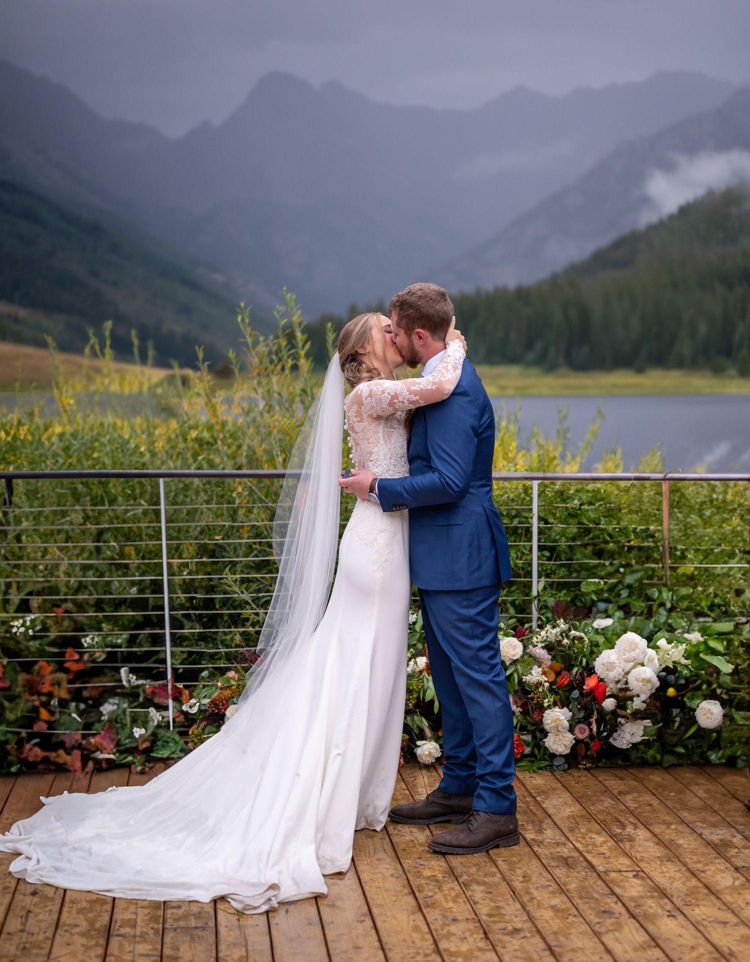 Wedding couple on wooden deck with mountain vista and flower arrangements at the wedding venue Piney River Ranch in Colorado.