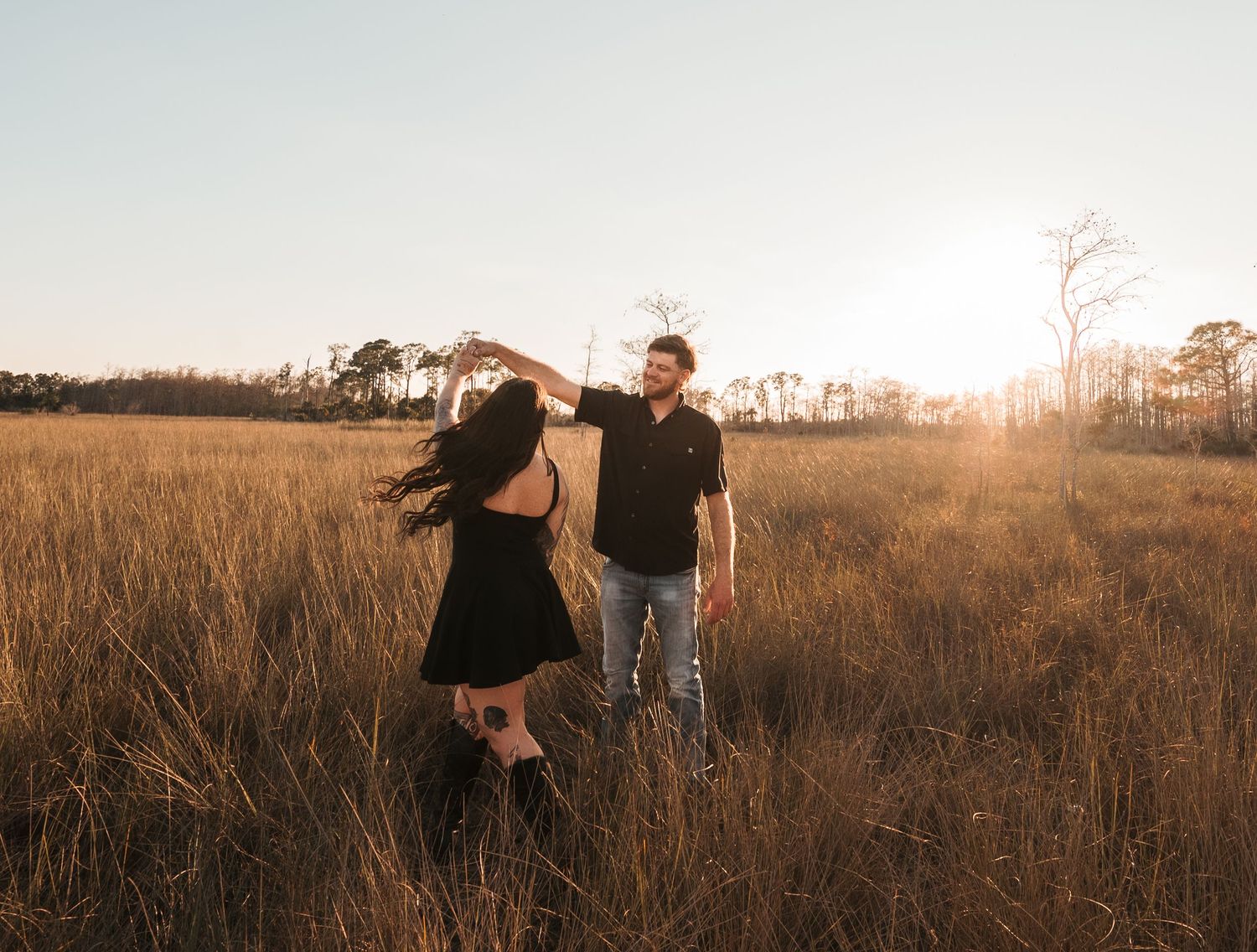 Two people walk together through a golden field at sunset creating a romantic silhouette against the warm sky.