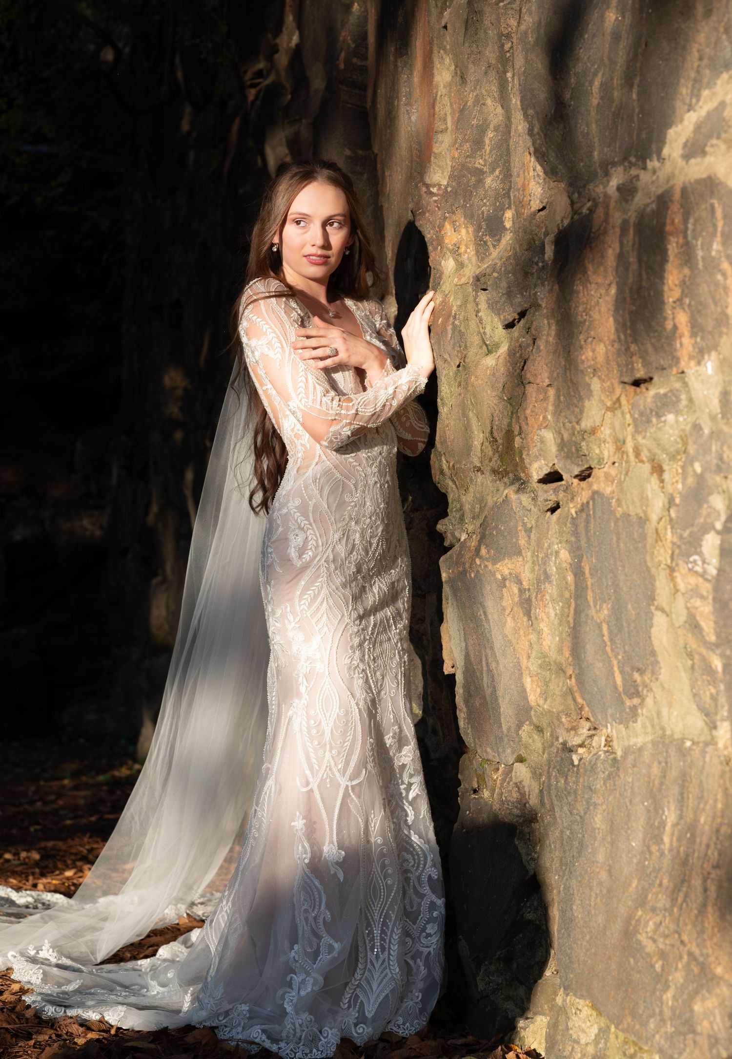Elegant bridal portrait in a lace gown against a rustic stone wall with flowing veil.