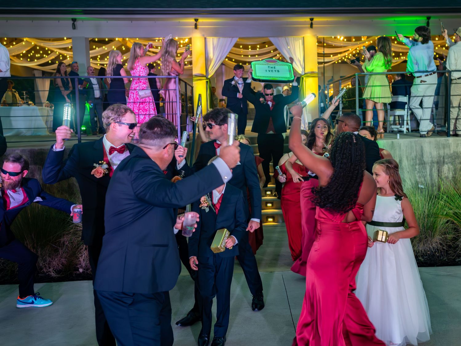 Wedding guests dance together on an illuminated dance floor with colorful lighting at an evening reception celebration.