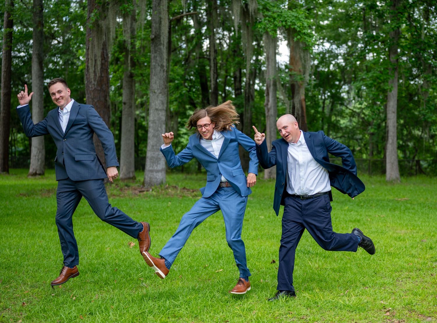 Playful groomsmen jumping and posing for fun photos on green lawn.