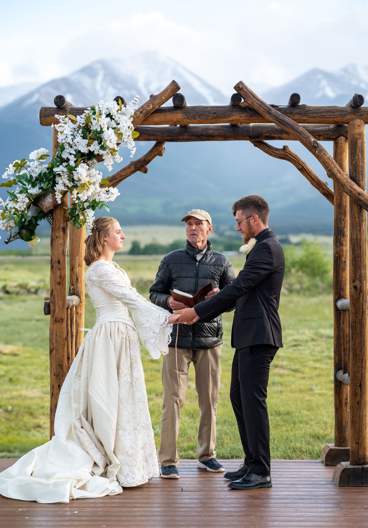 Wedding ceremony sequence showing couple and officiant beneath wooden arch with mountain backdrop at the Barn at Sunset Ranch wedding venue.