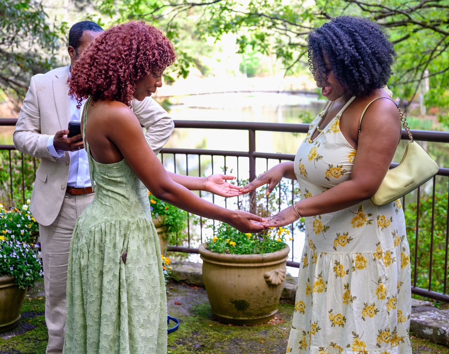 Two women examining a stone garden planter outdoors while a couple stands in the background near a railing.