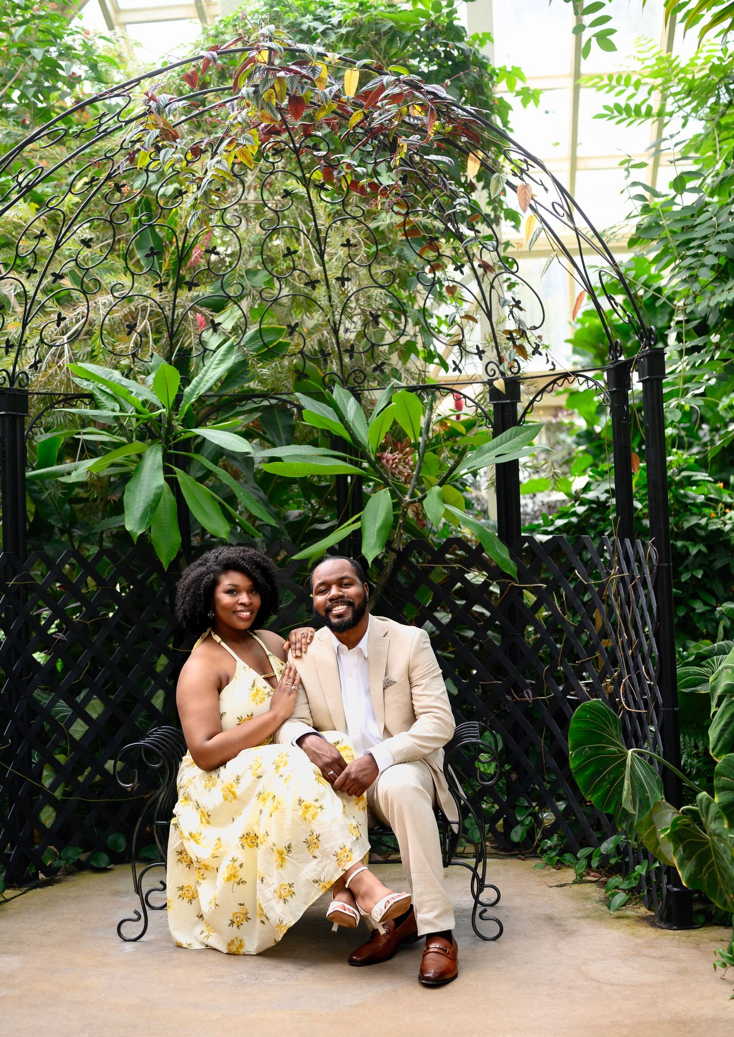 Couple posing together under an ornate iron arbor surrounded by tropical plants in a botanical garden.