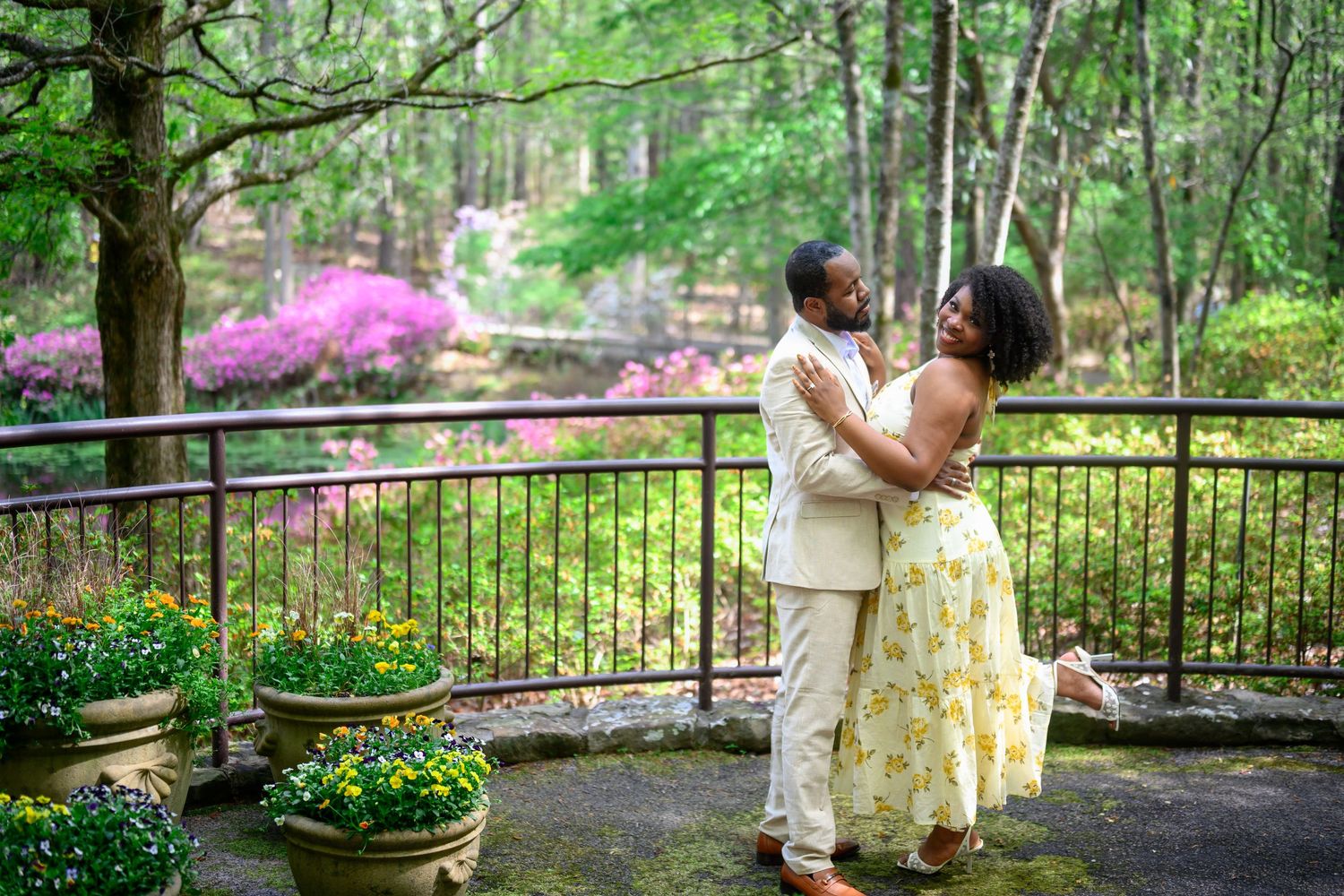 A happy couple embraces and dances joyfully in a scenic garden surrounded by blooming pink azaleas and green foliage.