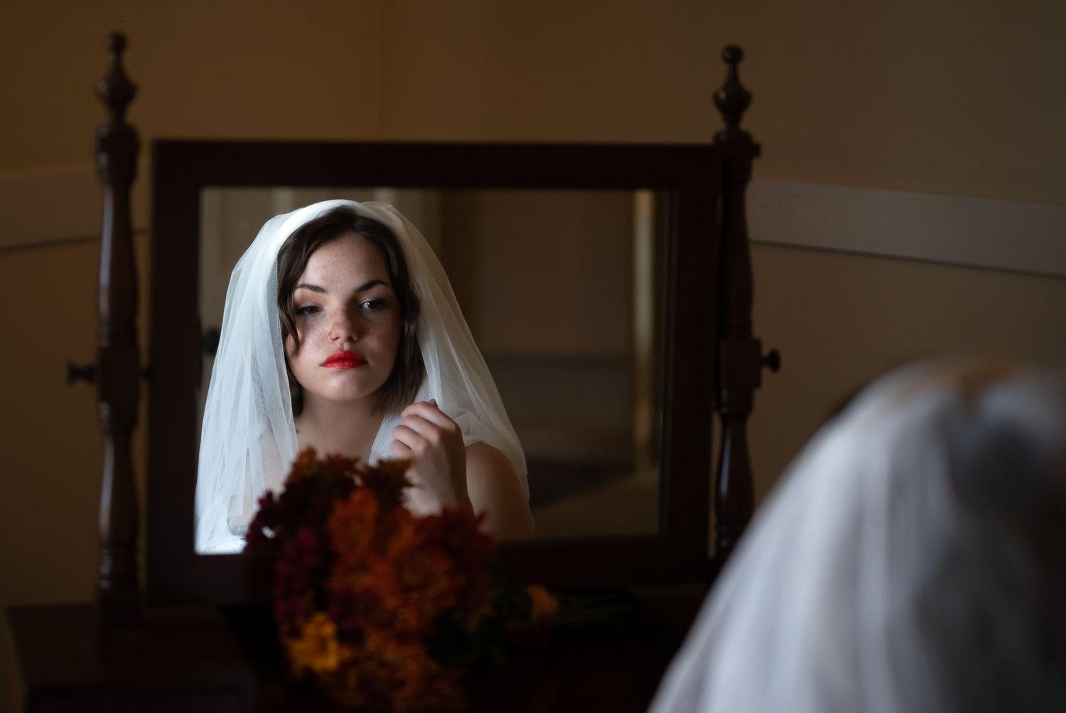 A woman sits and poses in front of a window while wearing a white wedding dress and veil.