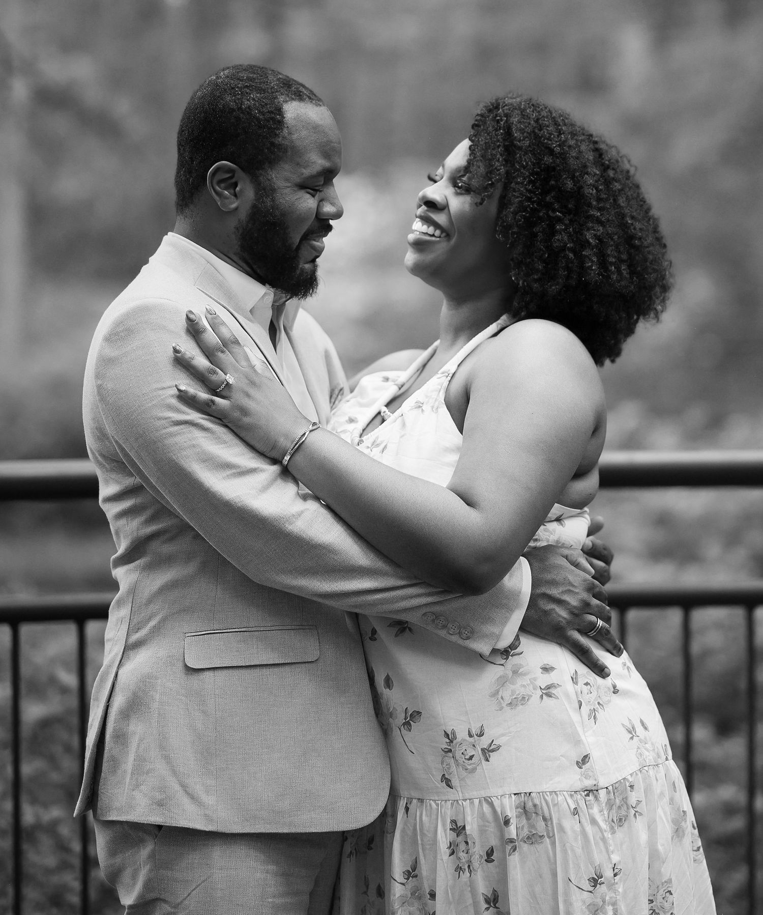 Black and white photo of a couple laughing and embracing near a decorative railing outdoors.