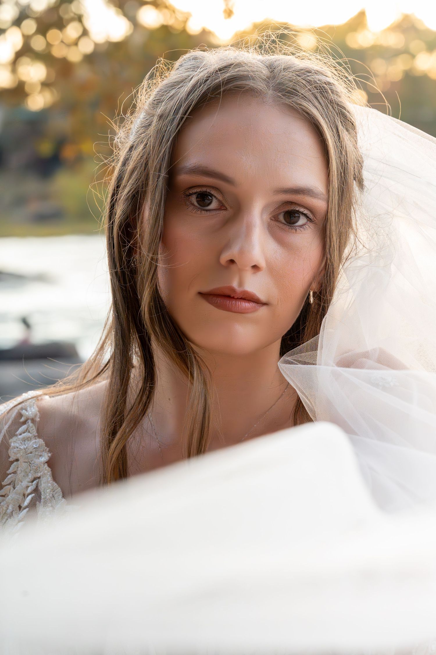 Close up portrait of bride wearing delicate lace gown and flowing veil in golden outdoor light.