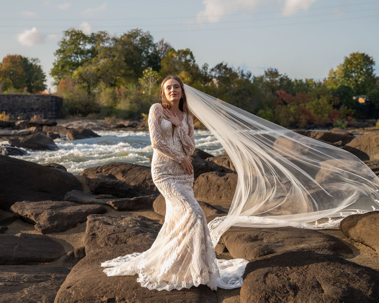 A long white veil flows dramatically in the wind as a bride poses on rocky terrain.