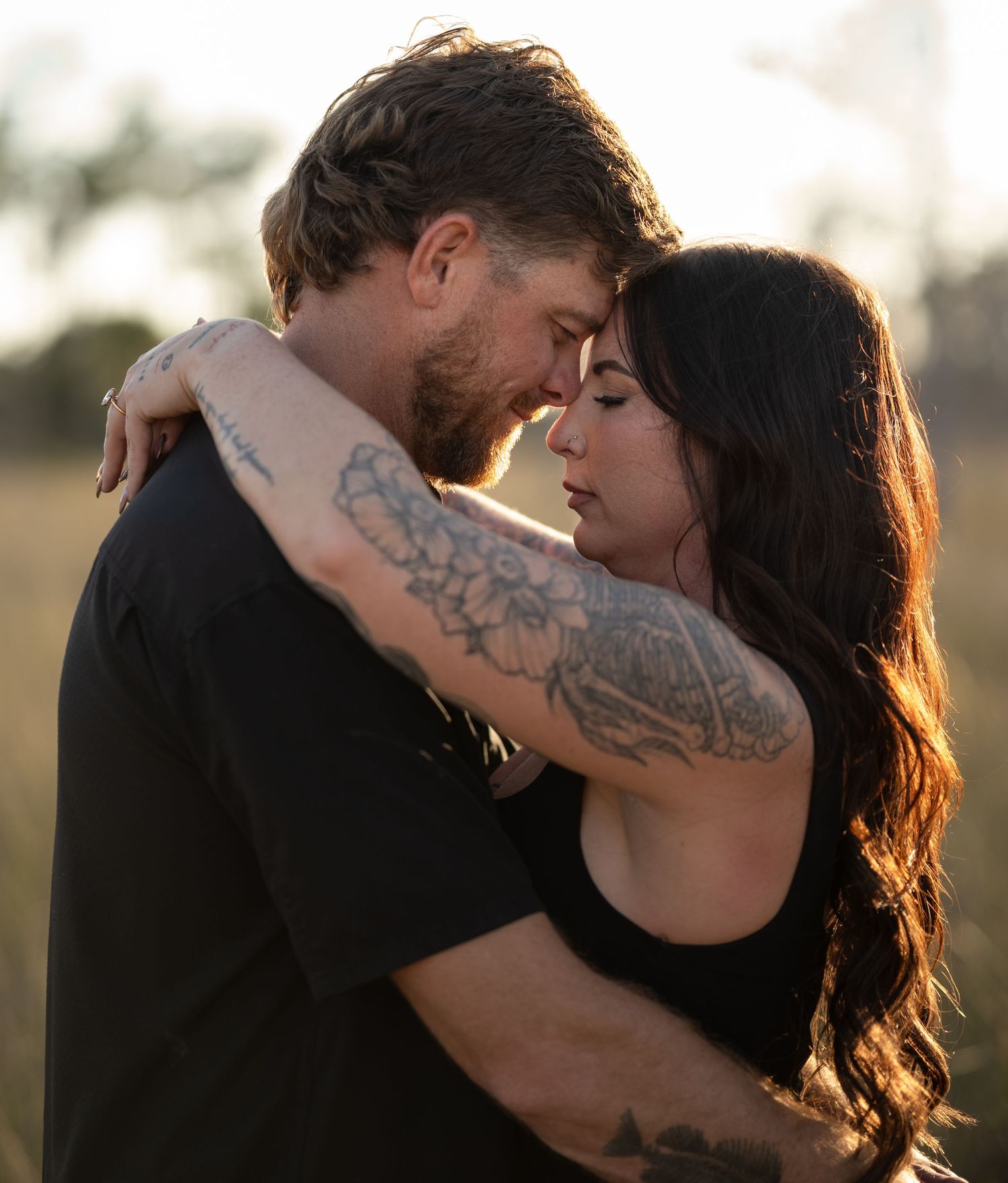 Intimate moment between couple with tattoos embracing outdoors in warm sunlight.