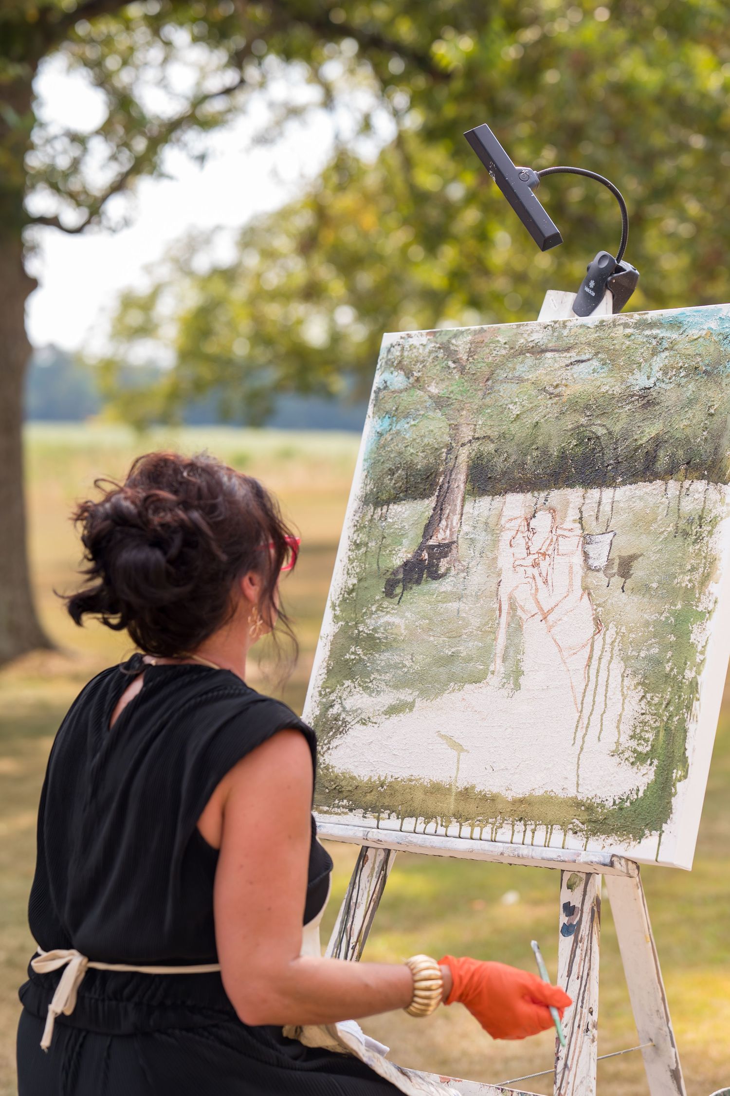 Artist painting at an easel outdoors in a natural setting with trees in the background.