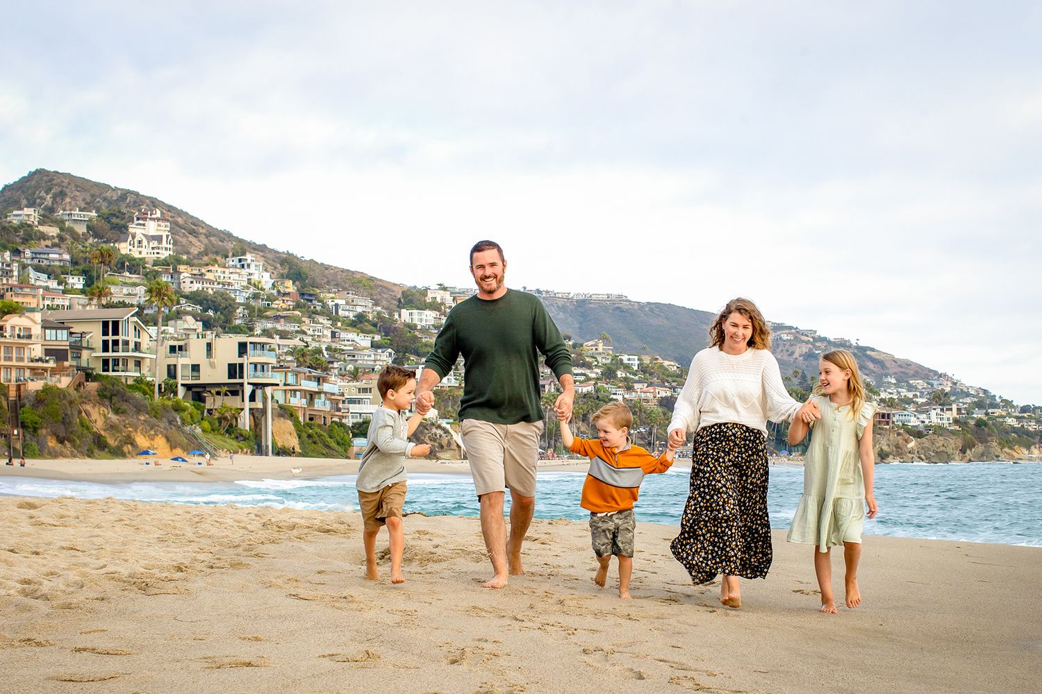 Family walking and playing together along a scenic coastal beach with mountains in the background.