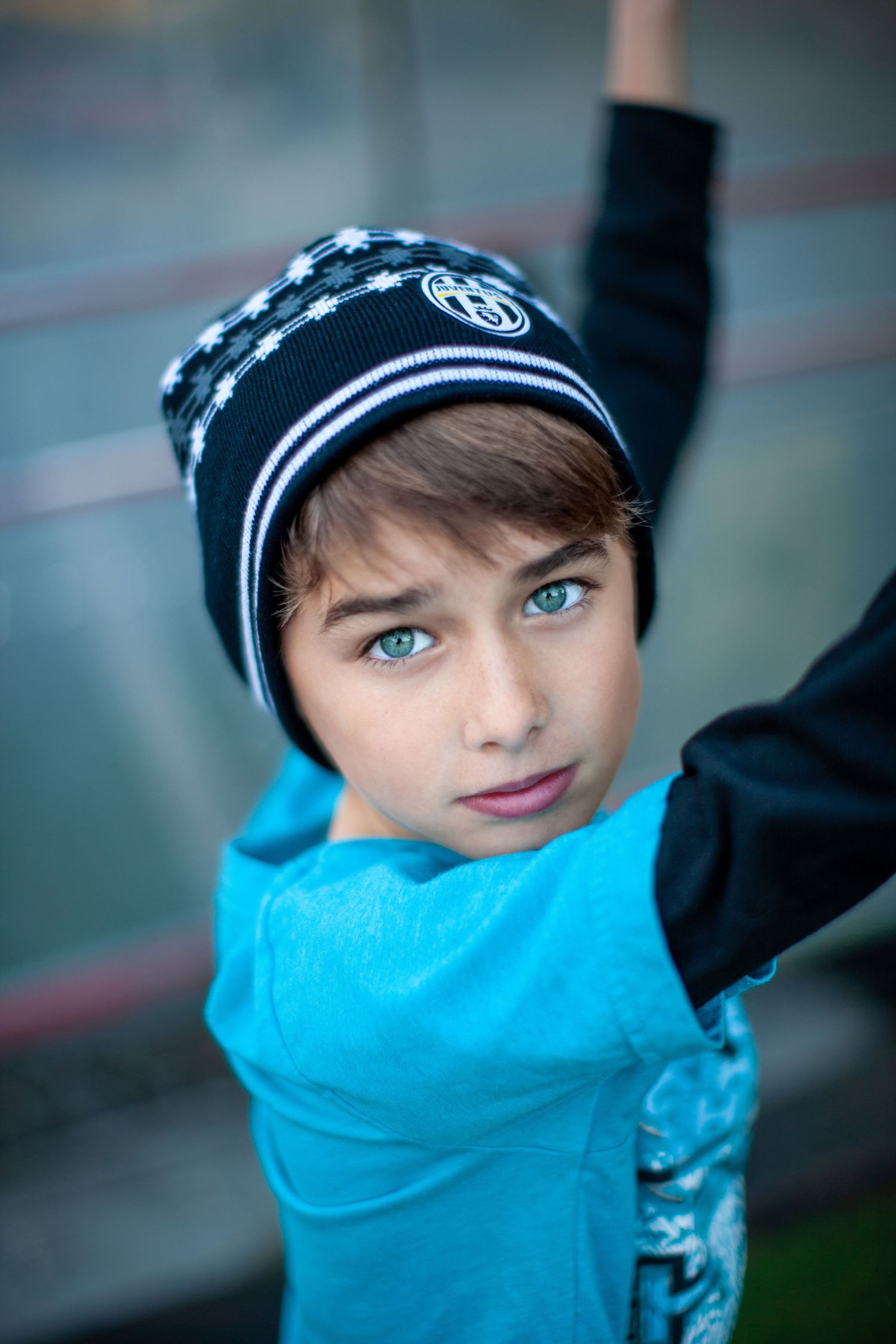 Person wearing a black knit hat and bright turquoise scarf gazes at the camera with striking blue eyes.