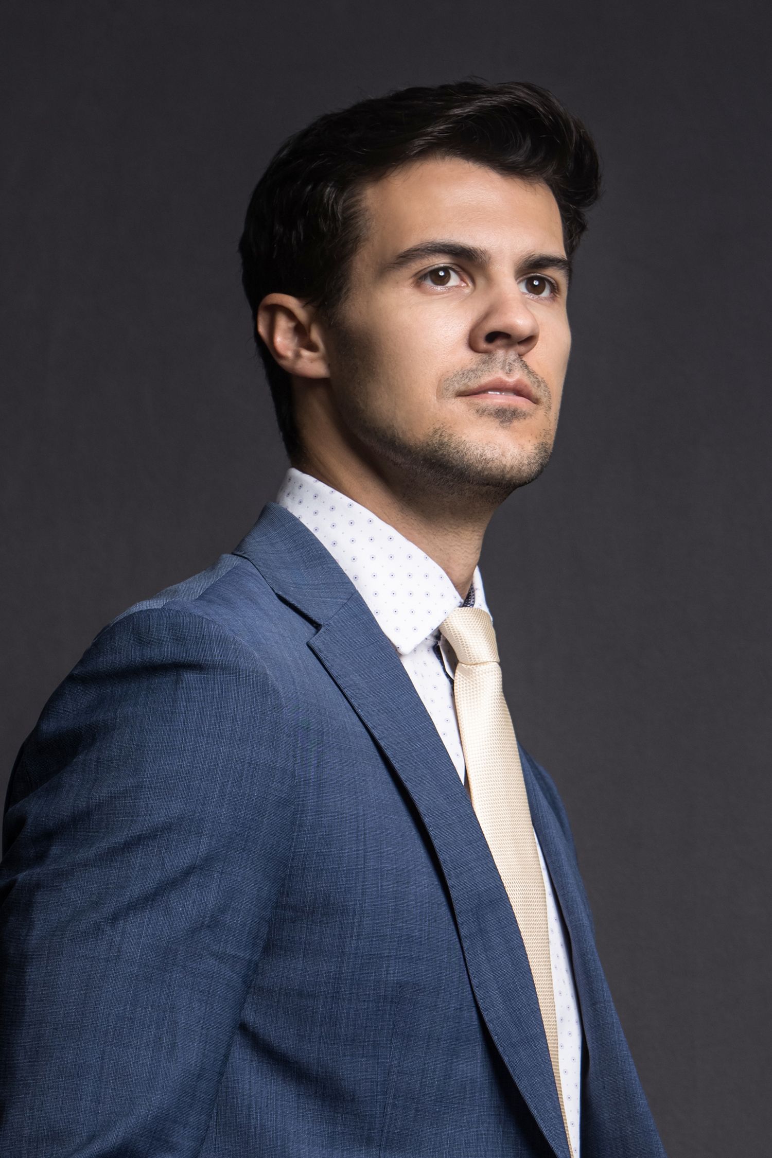 Professional portrait of person in navy suit against dark studio background.