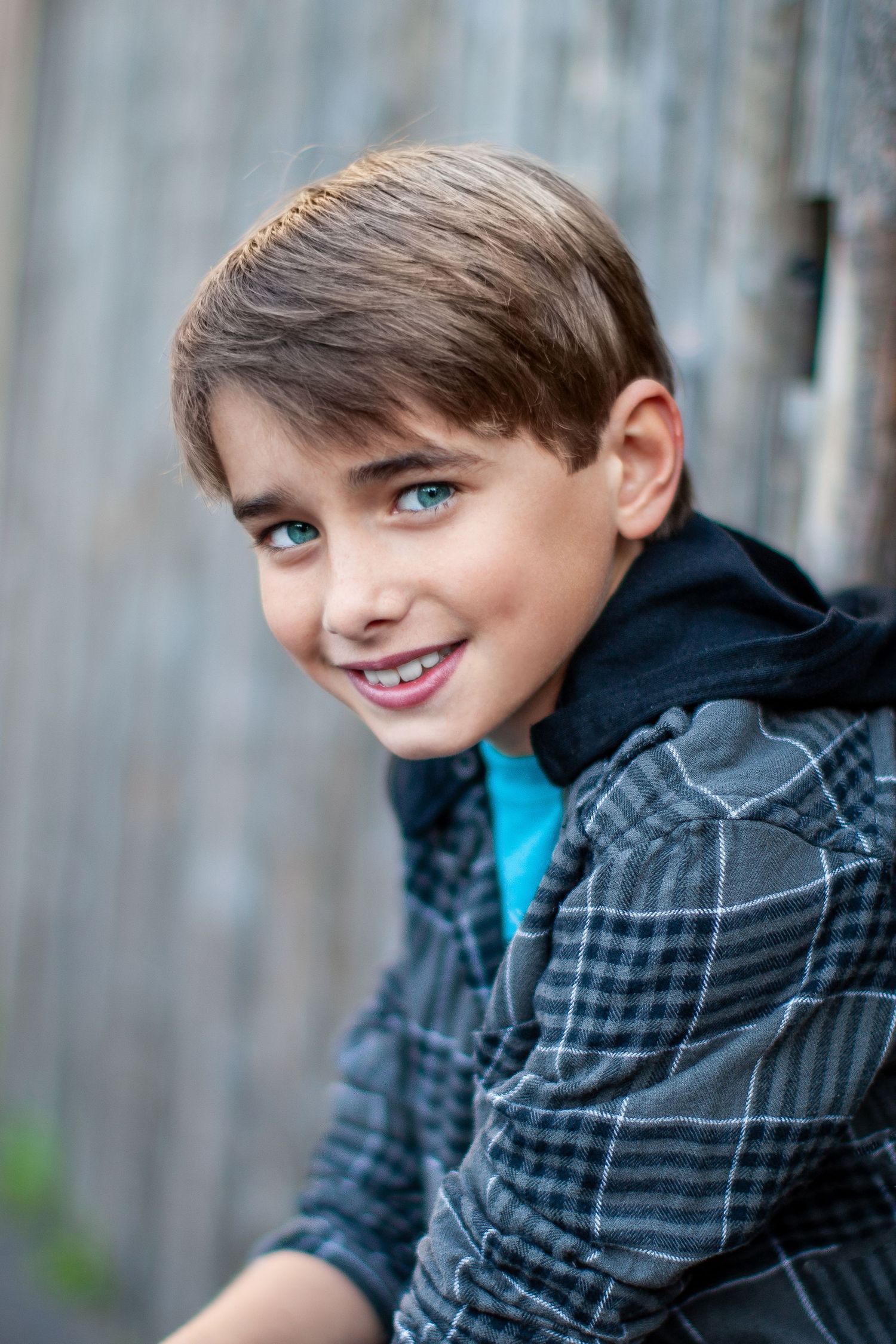 A smiling young person in a plaid hoodie strikes four different playful poses against a blurred background.